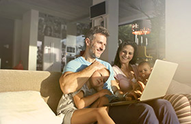 junges Ehepaar mit Kind und Baby auf der Couch vor dem Laptop