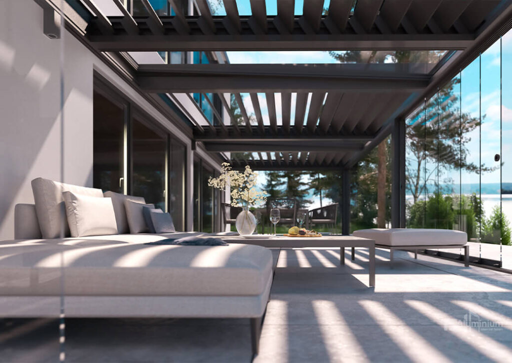 Moderne Außenterrasse mit stilvollen Terrassendächern, gepolsterten Liegestühlen, einem Tisch mit Weingläsern und Blumen sowie einem Blick auf Bäume und den blauen Himmel durch elegante Glaswände.