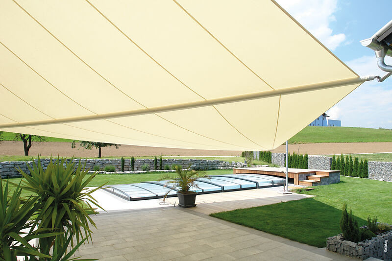 Ein großes, cremefarbenes, dreieckiges Sonnensegel, das einen Swimmingpool im Hinterhof mit einer Schiebeabdeckung beschattet.