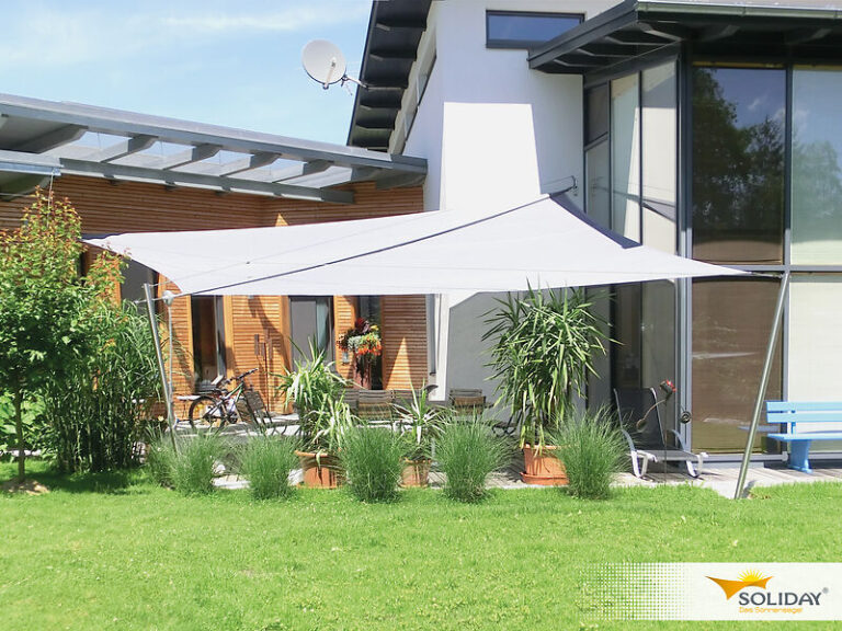 Ein weißes, rechteckiges Sonnensegel überspannt eine Terrasse neben einem Haus, unter der sich Topfpflanzen und Gartenmöbel befinden.